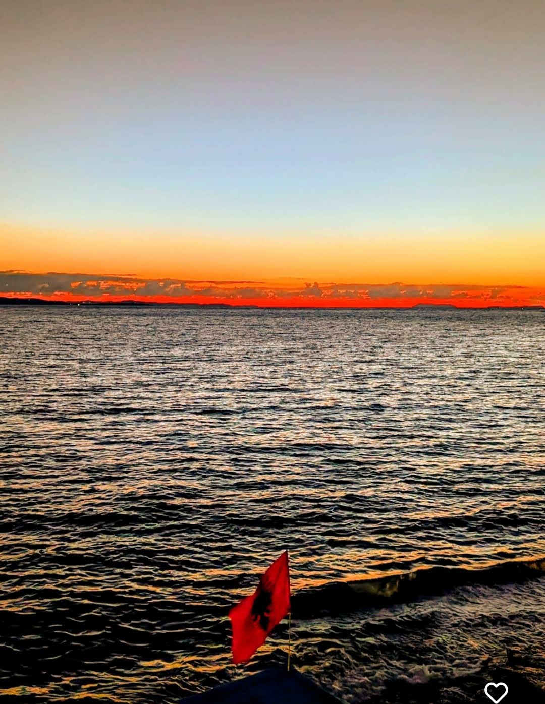 Albanian flag on the Sarandë shoreline at sunset over the Ionian