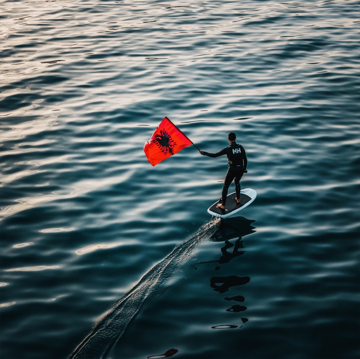 Wing foiler with Albanian flag on the Ionian Sea at sunset
